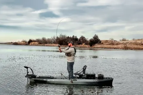 Pescatore su kayak con motore elettrico. Ottimo consiglio batteria motore elettrico per lunghe battute di pesca.