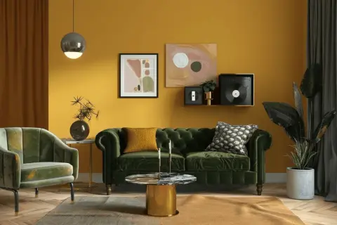 Ein Wohnzimmer mit senfgelben Wänden. Ein grünes Samtsofa und ein Sessel. Welcher Farbe passt zu Gold? Der goldene Couchtisch und Akzente im Bild zeigen, dass Grün und Gelb gut harmonieren.