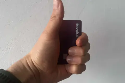 Dłoń trzymająca fioletową kartę Revolut, kciuk uniesiony w geście aprobaty.
