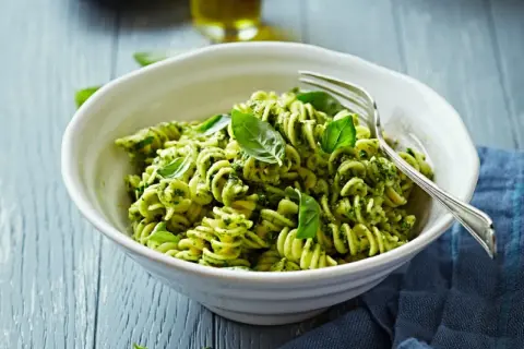 Eine Schüssel Fusilli-Nudeln mit grünem Pesto und frischem Basilikum, garniert mit einer Gabel.