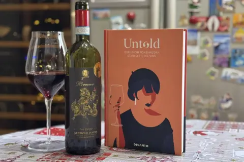 Un bicchiere di vino rosso Nebbiolo d'Alba, una bottiglia e un libro "Untold" sul vino. Le caratteristiche del Nebbiolo sono un viaggio affascinante.