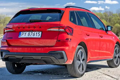 Czerwona Skoda Kamiq z polskimi tablicami rejestracyjnymi, zaparkowana nad wodą. Sprawdź atrakcyjną skoda kamiq cena!