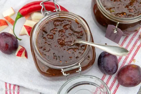 En burk med plommonchutney, perfekt för ett plommon recept. Äpplen, plommon och chili ligger bredvid.