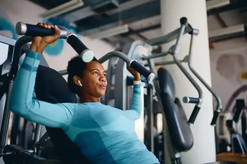 Frau trainiert richtig im Fitnessstudio an einer Brustpresse. Sie konzentriert sich auf die Bewegung und hört Musik über ihre Kopfhörer.