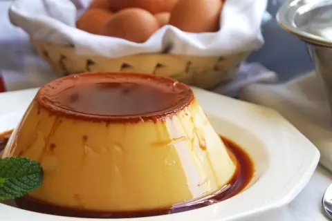 Delicioso flan de huevo de 1 litro, con caramelo líquido y una hoja de menta. En el fondo, huevos frescos en una cesta.