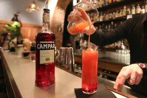Barman nalewa drink z dzbanka do szklanki z lodem. Obok stoi butelka Campari. To właśnie Campari co to za alkohol?