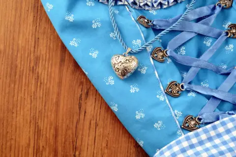 Ein Dirndl-Mieder mit Herzanhänger und Schnürung liegt auf Holz. Bald wird die Dirndlschürze gewaschen.
