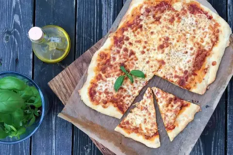 Pyszna margarita pizza z roztopionym serem i bazylią, obok oliwa i świeże liście.