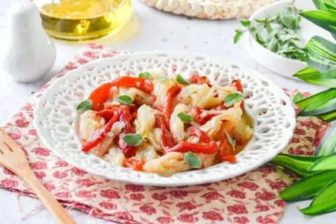 Deliciosa ensalada de bacalao con pimientos rojos asados y hierbas frescas, servida en un plato blanco decorado.