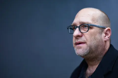 Portret mężczyzny w okularach, łysiejącego, z zarostem. Todd Hido w skupieniu.