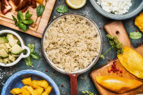 Perfekt gekochtes Quinoa in einer Pfanne, umgeben von frischen Zutaten wie Avocado, Mango und Tomaten.