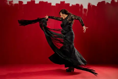 Bailarina de flamenco con mantón negro sobre fondo rojo vibrante.
