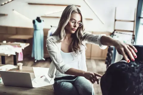Eine Designerin mit Brille misst Stoff für ihr nächstes Projekt im Bereich IU Modemanagement.