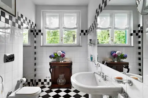 Un elegante bagno bianco e nero vintage con piastrelle a scacchi, un lavabo classico e un vaso di ortensie.