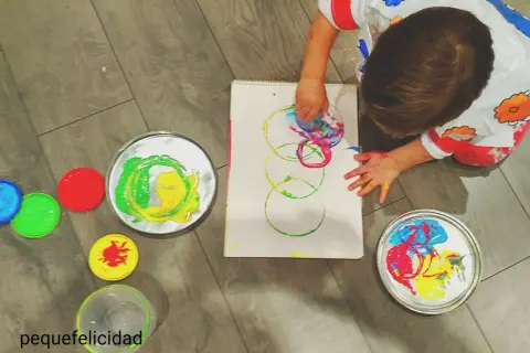 Niño pequeño creando arte con pintura de dedos. Lienzo con círculos de colores y recipientes de pintura.