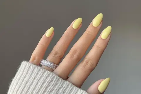 Dłoń z idealnymi, żółtymi pastelowymi paznokciami i błyszczącym pierścionkiem.