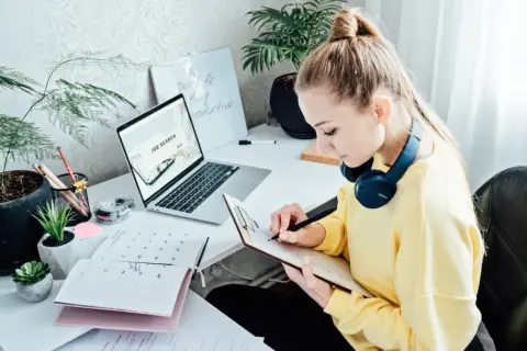 Kobieta pracuje nad CV, szukając pracy. Na biurku laptop z napisem "Job Search", kalendarz i notatnik.
