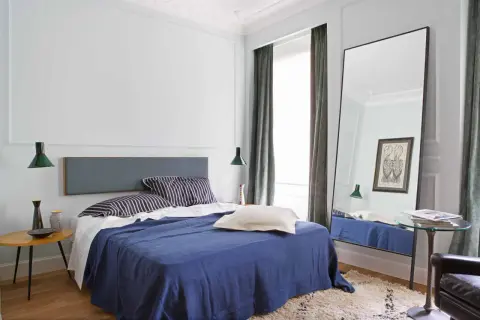 Modern mens bedroom ideas: a navy blue bed with striped pillows, a grey headboard, and a large floor mirror reflecting the room.