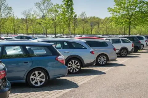 Amplio estacionamiento con coches alineados bajo árboles verdes. Ideal para saber dónde parcheggiare a Granada sin estrés.