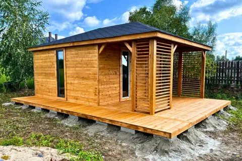 Drewniany domek narzędziowy z werandą, posadowiony na bloczkach betonowych. Solidne podłoże pod domek narzędziowy zapewnia stabilność.