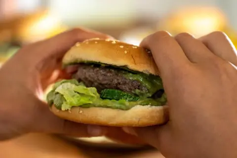 Hände halten einen saftigen Burger mit Hackfleisch. Ein köstliches Beispiel für Hackfleischgerichte, das zum Reinbeißen einlädt.