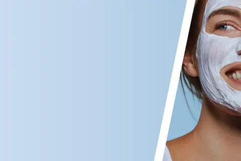 Mujer sonriente con mascarilla de arcilla blanca, disfrutando de un momento de cuidado facial.