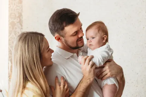 Uśmiechnięta mama i tata patrzą na swoje dziecko, które właśnie zaczyna rozpoznawać twarze.