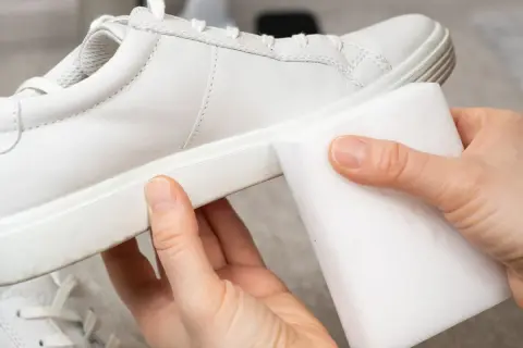 Manos limpiando zapatillas blancas piel con una esponja mágica. ¡Devolviendo el brillo a tus zapatos!