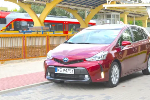Czerwony Toyota Prius Plus stoi na peronie obok pociągu.