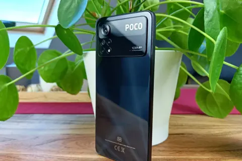 Czarny smartfon POCO X4 z potrójnym aparatem 108MP, otoczony zielonymi liśćmi rośliny.
