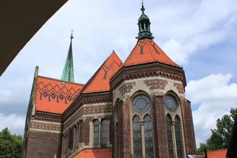 Suchanino kościół z zieloną wieżą i ceglaną fasadą, ozdobiony czerwonymi dachami i ozdobnymi oknami.