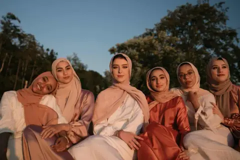Seis mujeres con hiyabs posan juntas. El tejido modal se arruga suavemente en sus vestidos, creando un efecto elegante bajo la luz del atardecer.