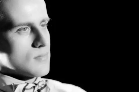 Portrait en noir et blanc d'un homme avec un nœud papillon, regardant sur le côté.