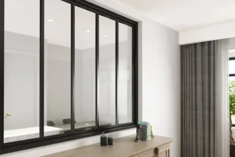 Amplio ventanal con **vidrio laminado de seguridad** y marco negro, reflejando una sala de reuniones. Cortinas grises y una planta adornan el espacio.