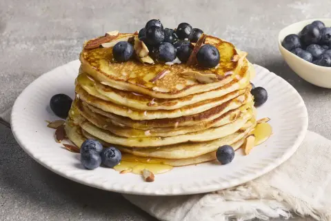 Stapel protein pancakes mit Magerquark, garniert mit Blaubeeren und Mandelsplittern, beträufelt mit Honig.