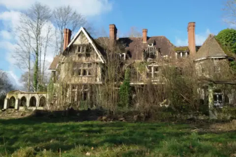 Maison abandonnée envahie par la végétation, un vestige de l'urbex Sarthe. Le toit est délabré, les fenêtres brisées, et la nature reprend ses droits.