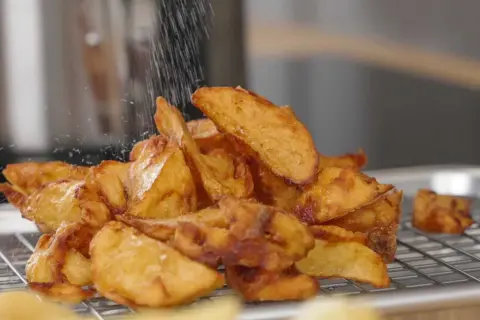 Krispiga potatisklyftor strös med salt efter frityr. Perfekt frityr temp för gyllene, läckra pommes.