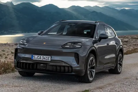 Szary Porsche Cayenne 2025 na kamienistej drodze z widokiem na góry i jezioro.