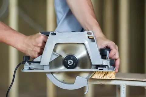 Mains d'un bricoleur utilisant une scie pour parquet stratifié, coupant une planche de bois.