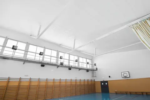 Techo de gimnasio con falso techo Heraklith, ventanas altas, canasta de baloncesto y equipamiento deportivo.