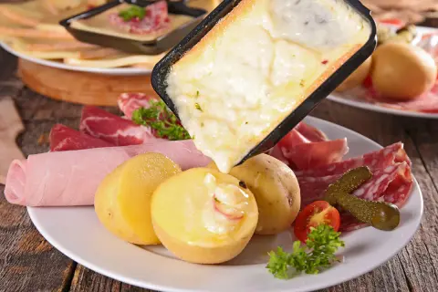 Raclette queso fundido cayendo sobre patatas, embutidos y pepinillos. ¡Una delicia para compartir!
