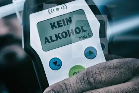 Dłoń trzyma alkomat z napisem "KEIN ALKOHOL" na wyświetlaczu.