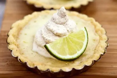 En liten citron key pie med en klick grädde och en limeklyfta.