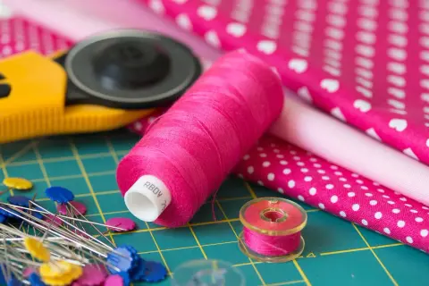 Różowe nici, szpilki, rolka do tkanin i materiały z wzorami – idealny zestaw do szycia z tkaniny **non woven**.