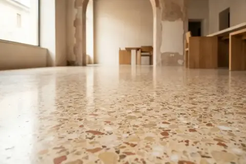 Pavimento lucido in cocciopesto veneziano, con riflessi di luce e mobili in legno sullo sfondo.