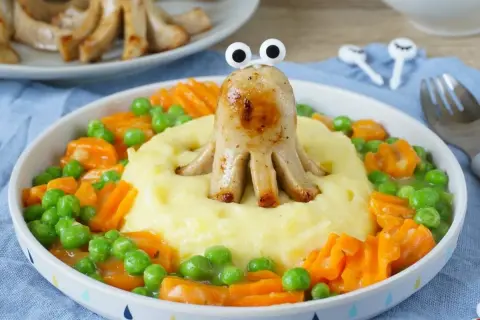 Ein lustiges gesundes Abendessen für Kinder: Würstchen-Oktopus auf Kartoffelbrei mit Erbsen und Karotten.