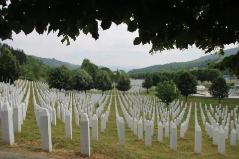 Enormt fält med vita gravstenar, en påminnelse om folkmordet i Srebrenica. Grönskande kullar i bakgrunden.