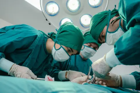 Zespół chirurgów w zielonych fartuchach i maseczkach przeprowadza operację zastawki serca. Skupienie na twarzach, precyzja ruchów.
