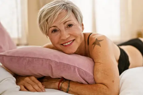 Lächelnde Frau mit kurzem blonden Haar und einem Stern-Tattoo auf der Schulter, das zeigt, dass Tattoos im Alter zeitlos sind.