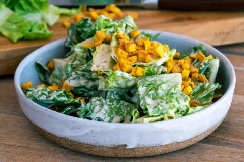 En skål med krispig romansallad, rikligt täckt med krämig caesarsallad dressing och toppad med gyllene krutonger.